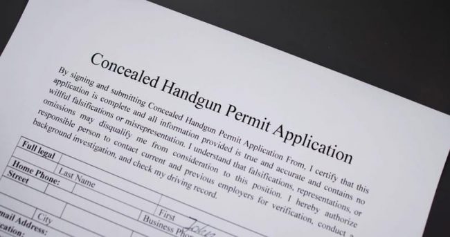concealed-handgun-permit-application A close-up shot of a "Concealed Handgun Permit Application" form lying on a dark surface, showing the title and the personal information fields at the bottom.