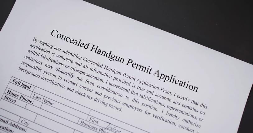 concealed-handgun-permit-application A close-up shot of a "Concealed Handgun Permit Application" form lying on a dark surface, showing the title and the personal information fields at the bottom.