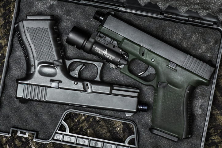 Top-down view of two semi-automatic pistols resting inside a protective foam-lined hard case; one handgun features an olive green frame equipped with a tactical weapon light.