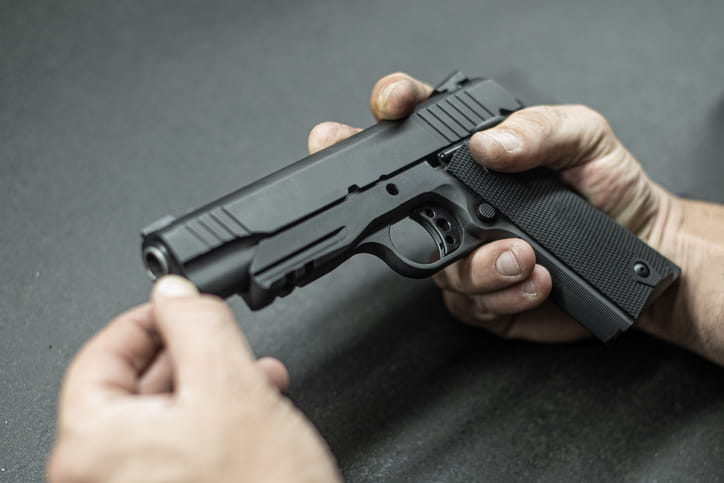 Close-up of hands holding a black semi-automatic handgun on a dark surface